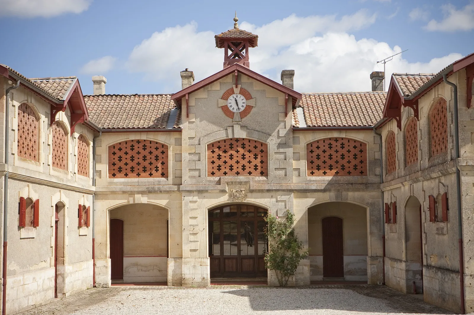 Interior courtyard of Château Lanessan in Bordeaux featuring stone stables with red wooden doors and a central clock face