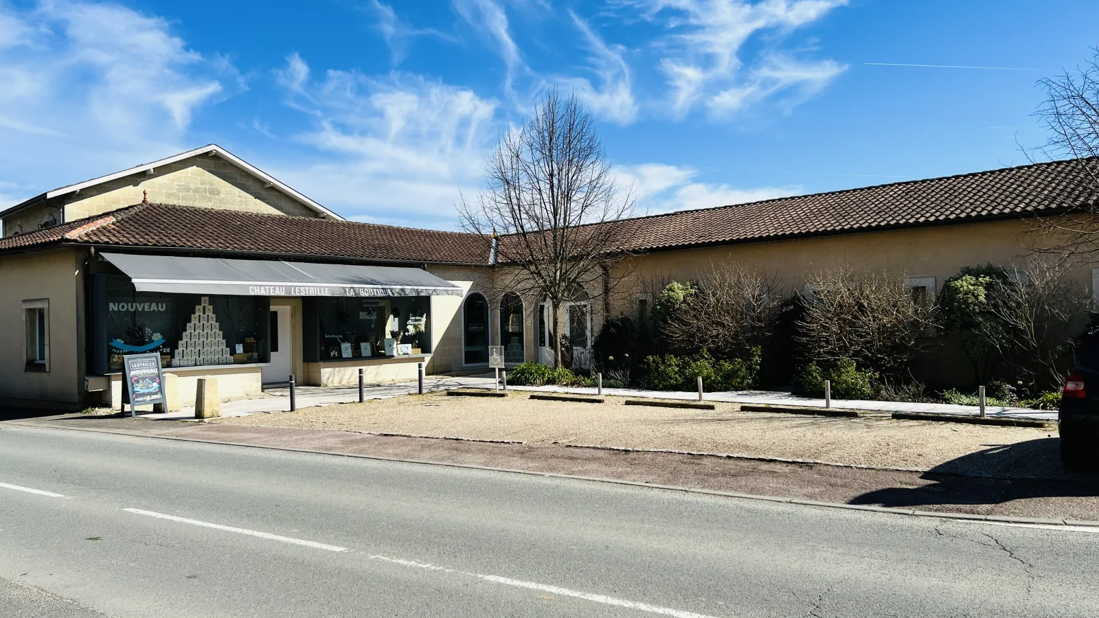 Château Lestrille in Bordeaux featuring a shop storefront, tile roof, paved courtyard and bare trees under blue sky