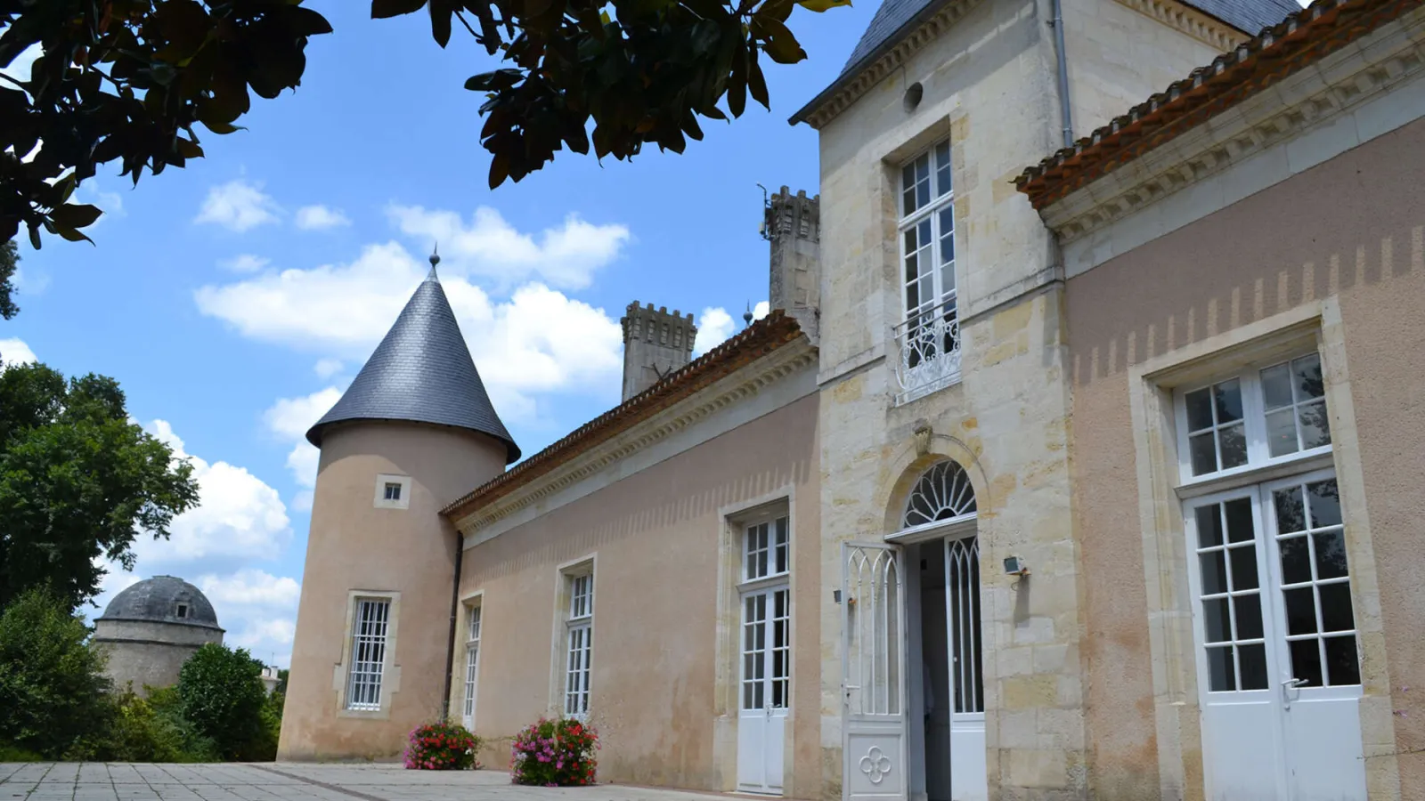 Facade of Château Lescombes, a contemporary art center in Bordeaux, featuring its distinctive round tower, white windows, and beige stone walls under a blue sky.