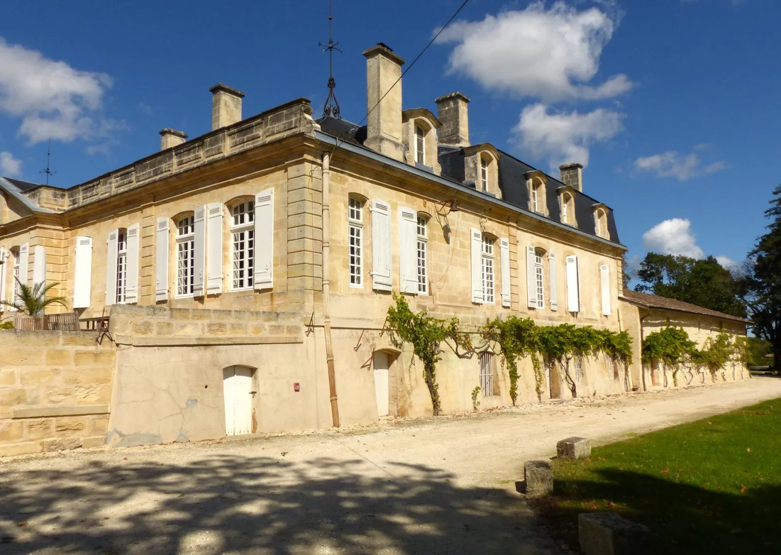 Château Sainte Barbe in Bordeaux, a classical stone manor house with mansard roof, white shuttered windows, and surrounding green grounds.