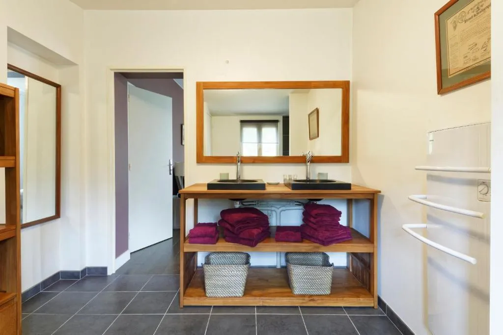 Modern bathroom with double sink and wooden-framed mirror, organized storage with burgundy towels and woven baskets, at Bastide de Siran in Bordeaux