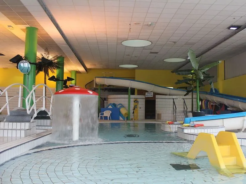 Indoor children's swimming pool at Pessac Water Sports Stadium in Bordeaux, featuring a yellow slide, green cactus fountain, and water play equipment
