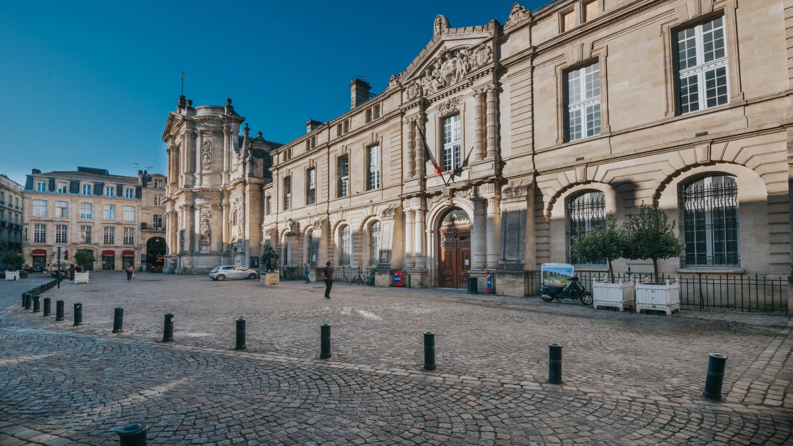 Paved square in Bordeaux featuring Notre-Dame Church and historic stone buildings under clear blue sky