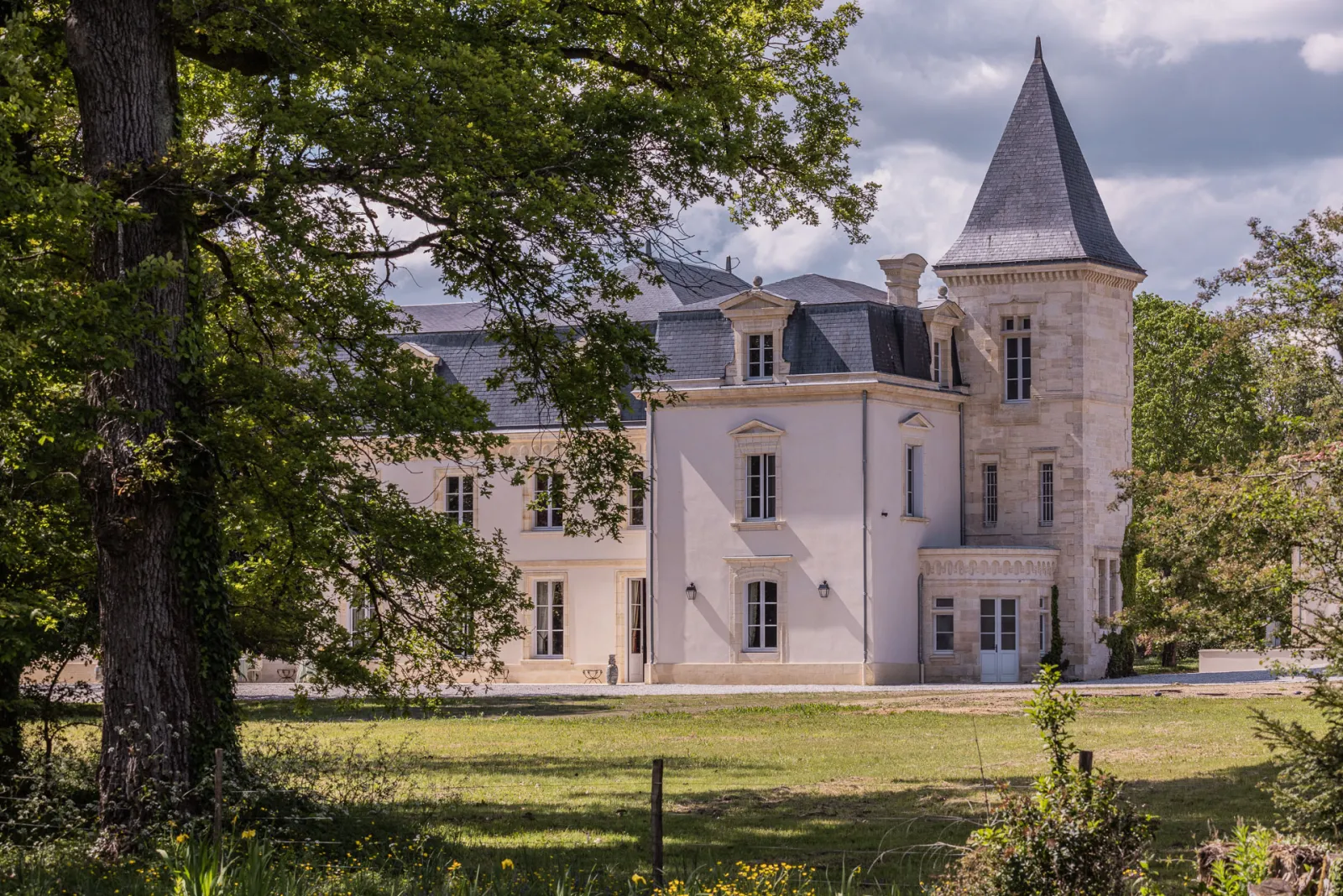 Château Sénéjac, a pink manor house with pointed turret surrounded by greenery and ancient trees near Bordeaux