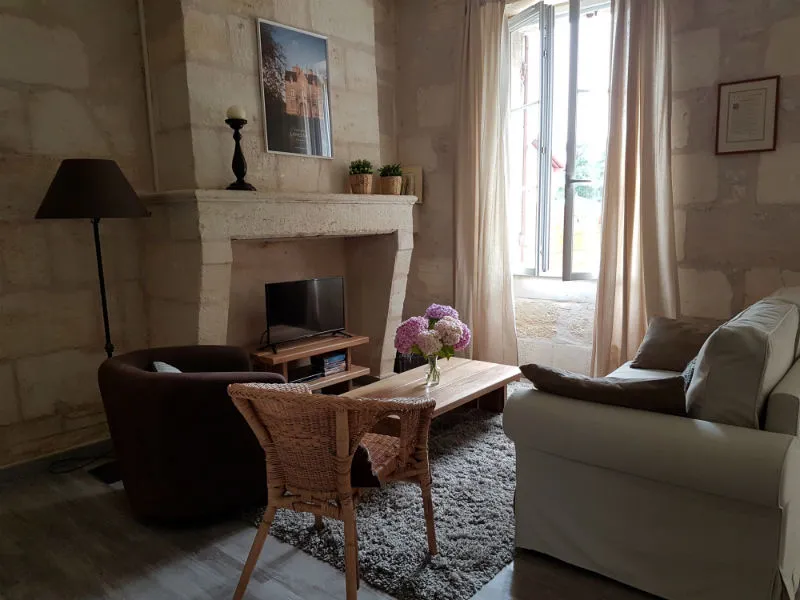 Elegant living room at Bordeaux's Maison des Hôtesses featuring a stone fireplace, classic furnishings, glass doors opening to a garden, and refined décor.