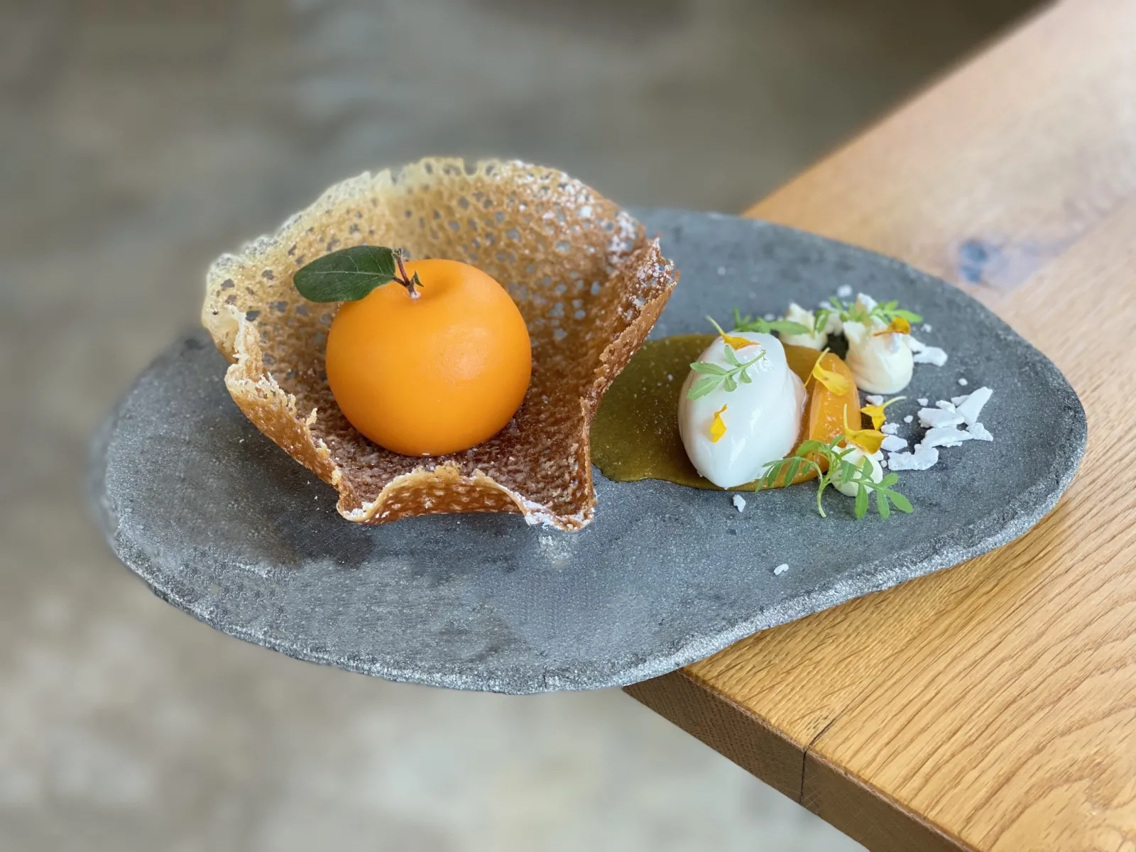 Gourmet plate featuring a crispy nest-shaped pastry with an apricot egg, served with cream quenelle, jelly and microgreens on a grey slate at Bordeaux