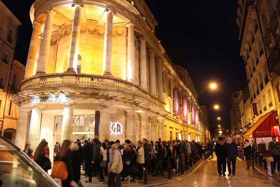 Queue of moviegoers outside the illuminated Méga CGR Le Français cinema in Bordeaux, featuring neoclassical architecture with prominent columns