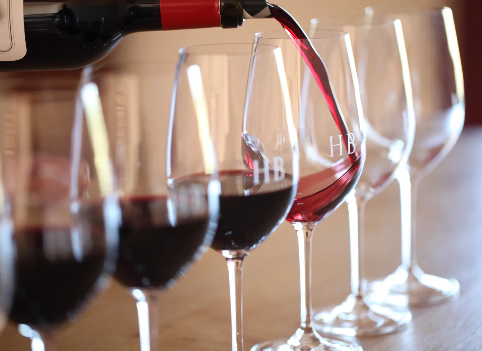 Wine tasting at Château Haut-Bailly in Bordeaux: pouring red wine into HB-branded glasses with multiple glasses lined up containing red wine.