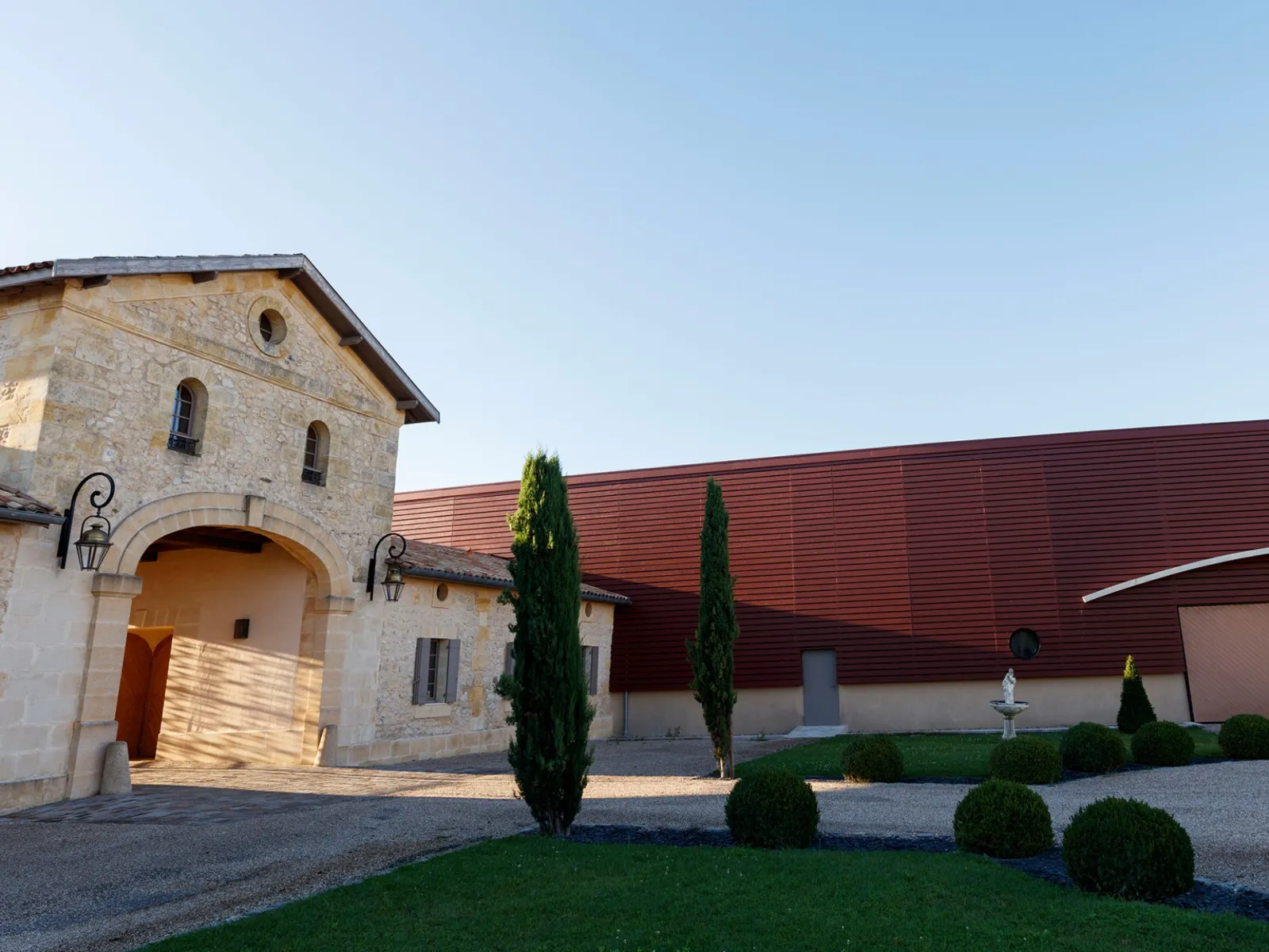 Château du Lort in Bordeaux: stone facade with arched gateway and red roof, surrounded by cypress trees and landscaped garden