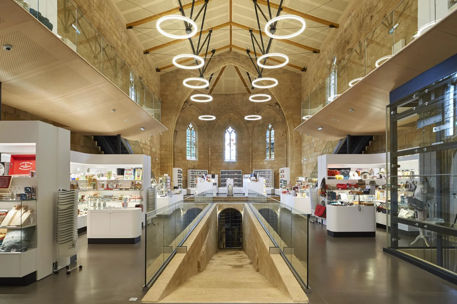 Modern bookstore interior housed in a decommissioned church at Les Cordeliers in Bordeaux, featuring stone vaults, stained glass windows, circular LED lighting, and white sales counters