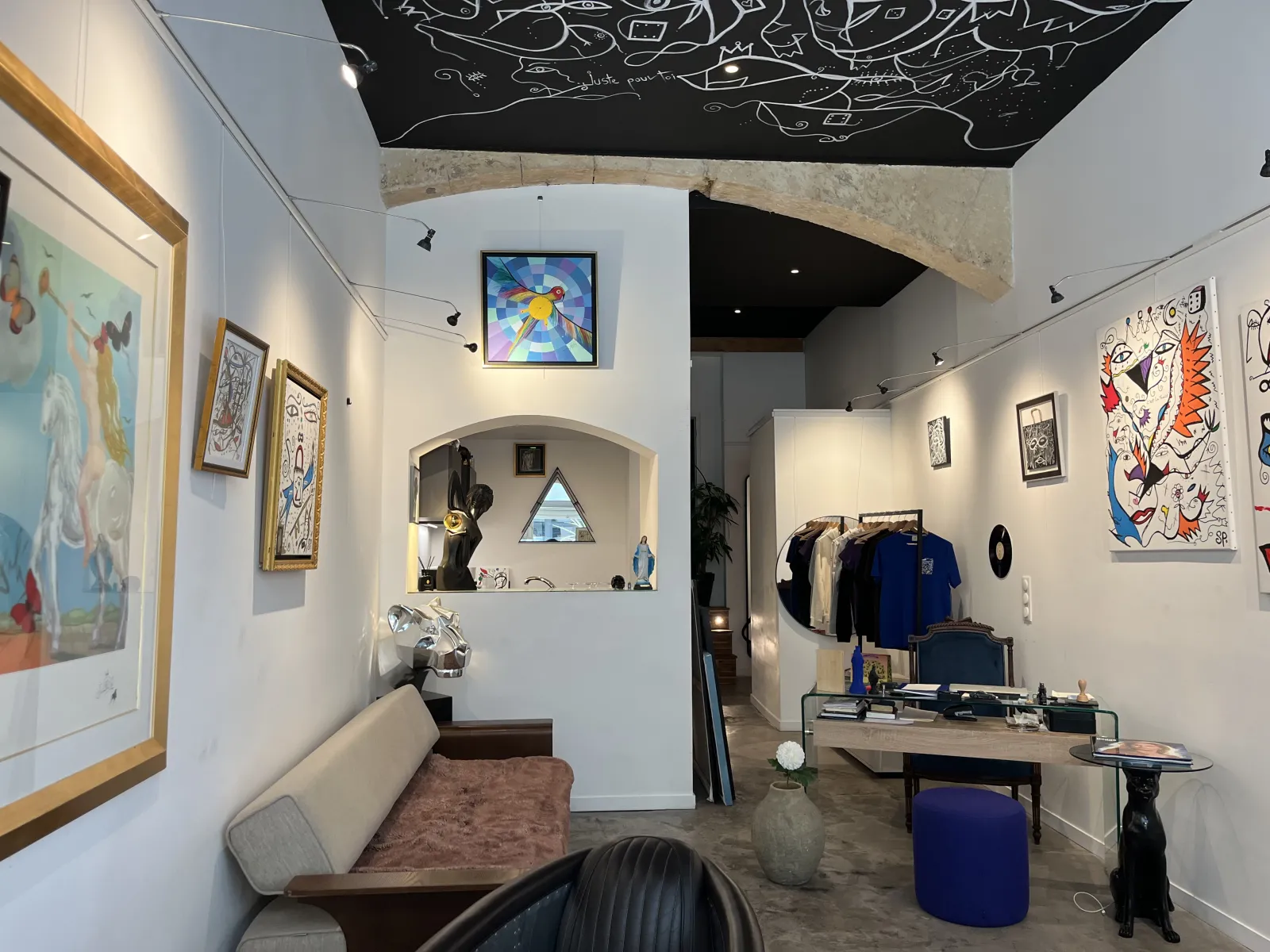 Interior view of SP Pour toi gallery in Bordeaux featuring contemporary artwork, displayed clothing, designer furniture, and artistic decorative elements on walls and ceiling.