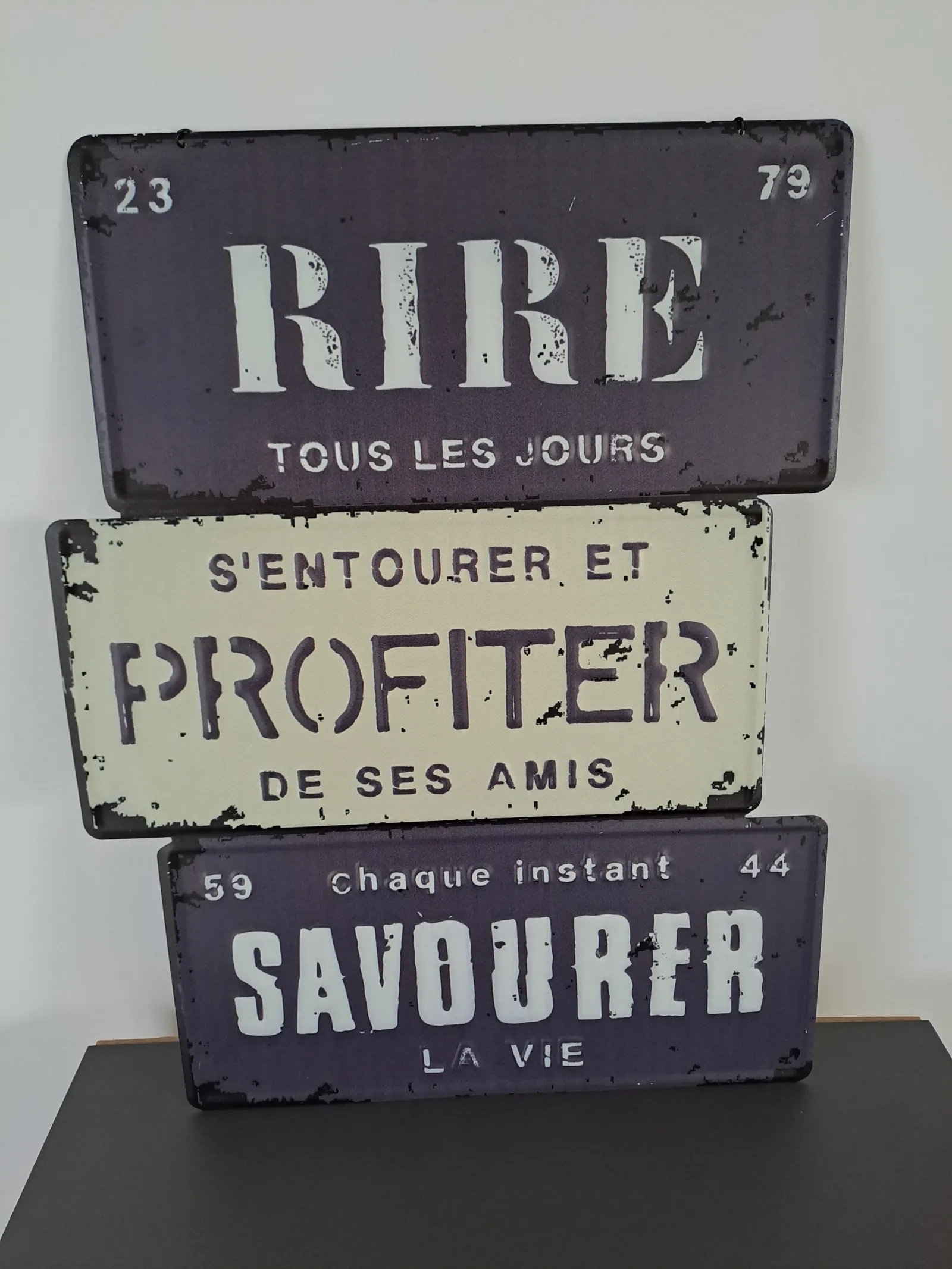 Three stacked vintage French enameled signs displaying motivational messages: 'Laugh every day', 'Surround yourself and enjoy your friends', 'Savor life every moment'. Antique wall decoration with retro style and weathered patina.
