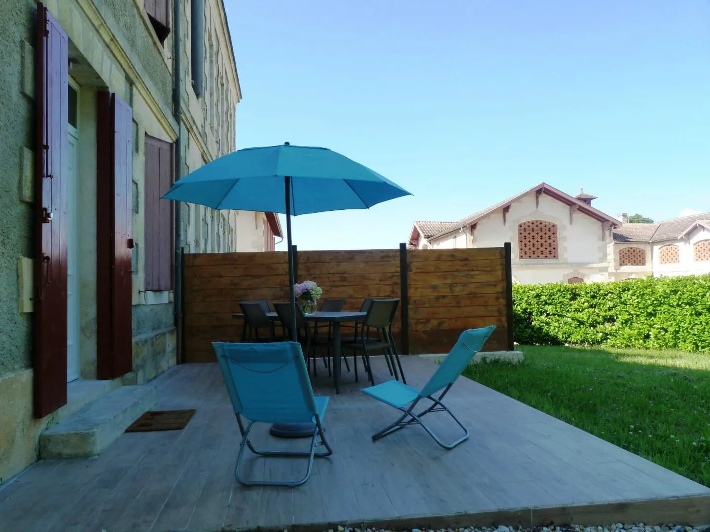 Sunny terrace at the Maison des Hôtesses in Bordeaux featuring blue loungers, blue parasol, garden furniture and wooden fence overlooking a green garden and neighboring houses