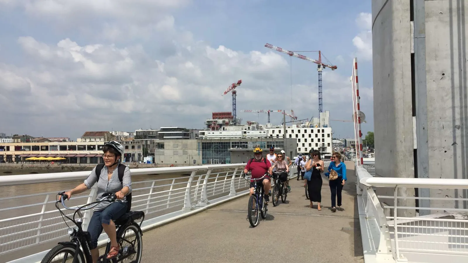Cyclists and pedestrians crossing the Jacques Chaban Delmas Bridge in Bordeaux, with views of the Garonne River and construction cranes in the background