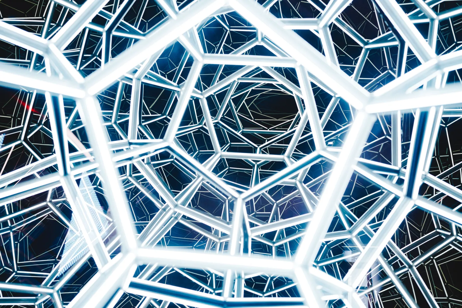 Blue and white neon tubes creating an interconnected geometric network pattern against a black background at Bordeaux's Museum of Illusion