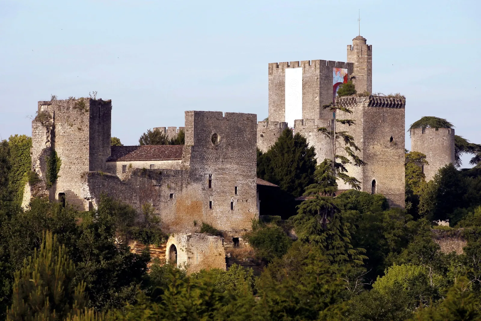 View of Château de Roquetaillade near Bordeaux featuring stone towers, crenellated walls, and surrounding vegetation under clear skies.