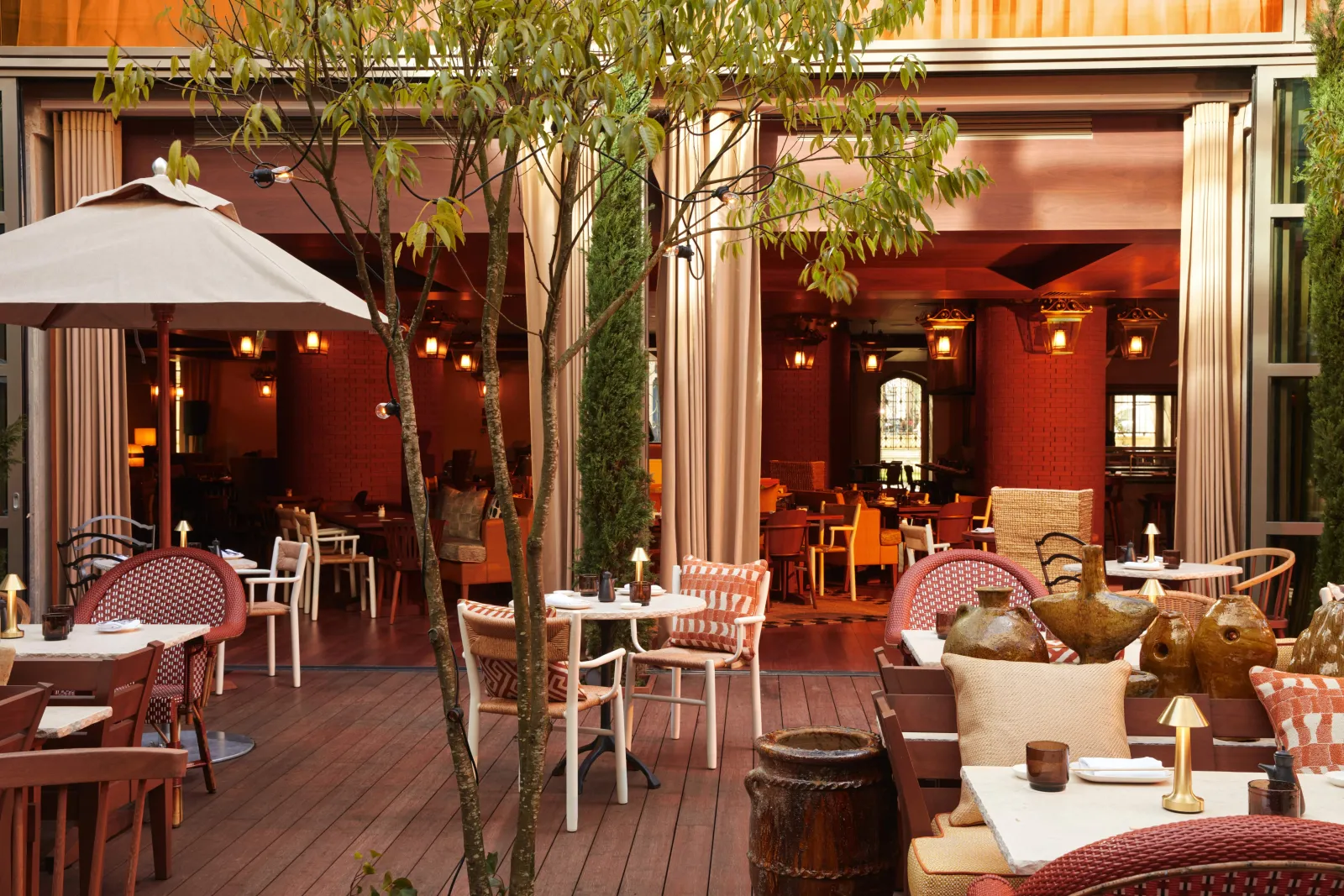 Elegant outdoor terrace of Morimoto restaurant in Bordeaux featuring red and white designer furniture, trees, umbrella, and modern red-walled interior with warm lighting.