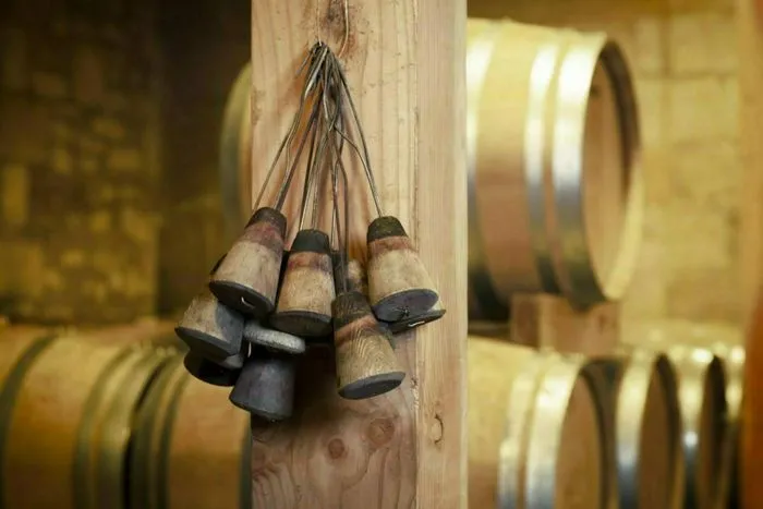 Vintage harvest bells hung from wooden beam in a wine cellar with oak barrels in the background, during the Open Doors of Castillon Côtes de Bordeaux châteaux