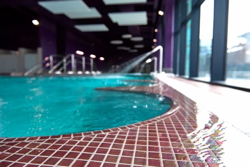 Modern indoor swimming pool with turquoise water, red tile edging, ambient lighting and large windows overlooking the outside at La Calinésie Aquatic Center