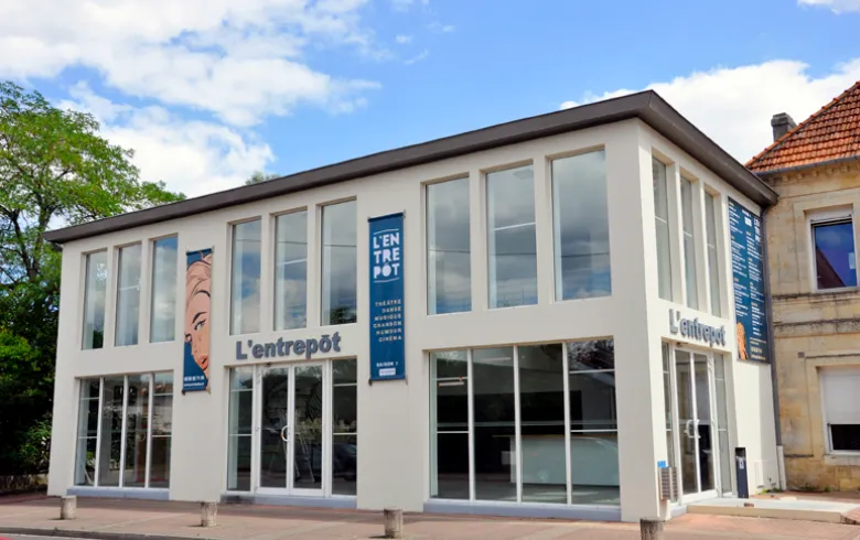 L'Entrepôt du Haillan, a modern white building with large glass windows and blue signage, located in Bordeaux, serving as a cultural and exhibition venue.