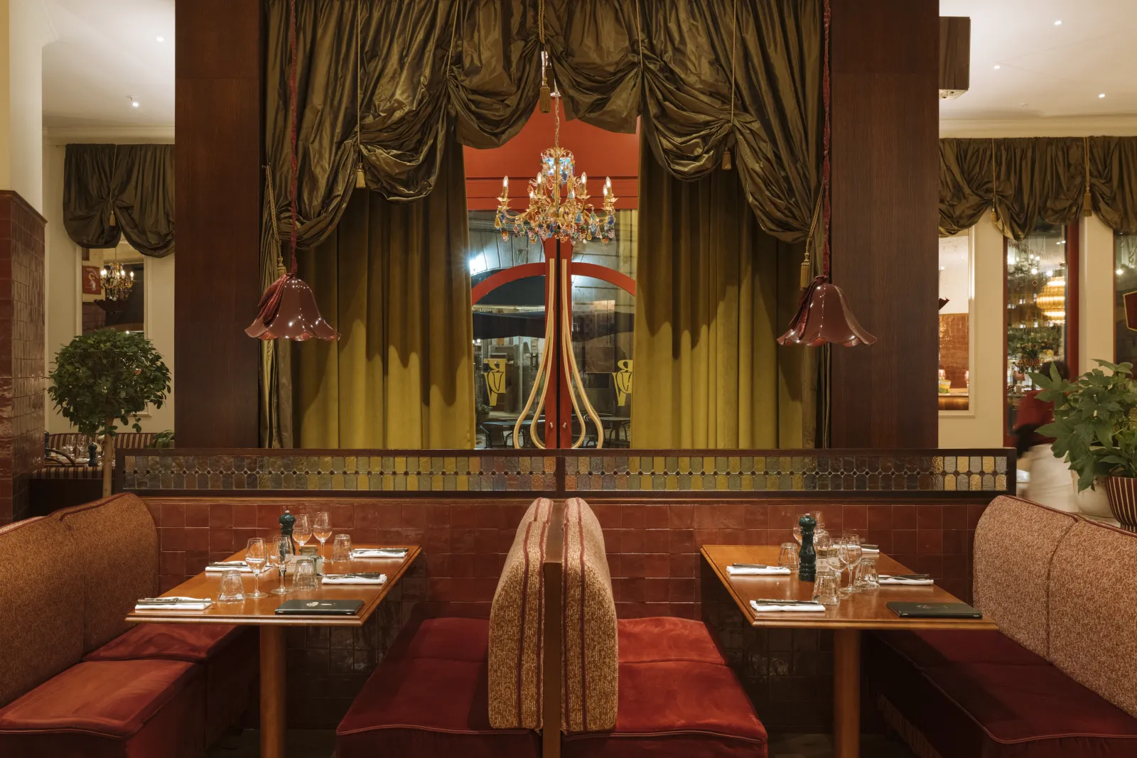 Elegant dining room of Brasserie Vinatier in Bordeaux featuring red and gold banquettes, wooden tables, golden drapes, crystal chandelier, and large windows overlooking the street.