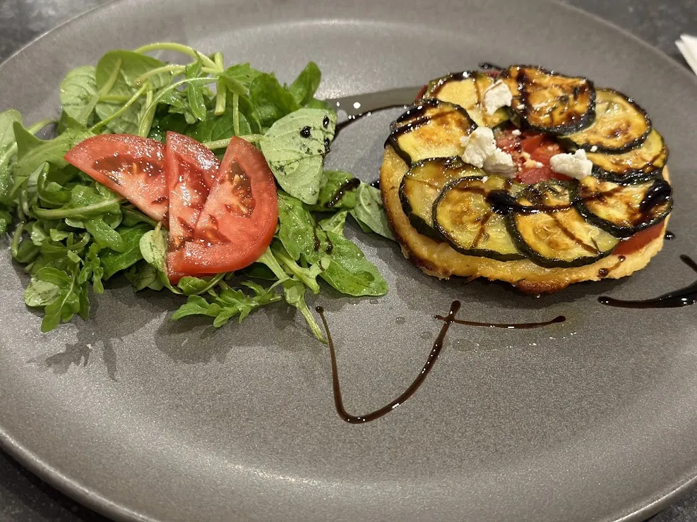 Gourmet plate featuring fresh green salad with tomato on the left, and a toasted open-faced sandwich topped with caramelized eggplant slices and white cheese on the right, garnished with balsamic reduction.