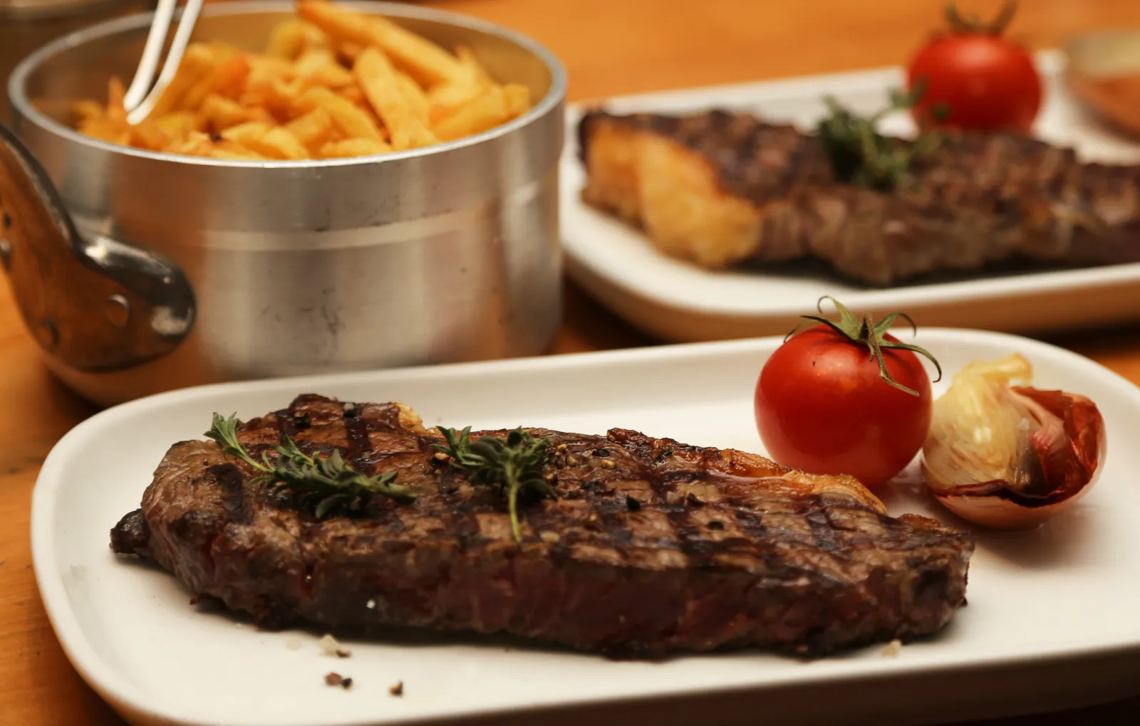 Grilled steak plate garnished with rosemary and tomato, served with fries in a metal basket and side dishes at Brasserie Bordelaise