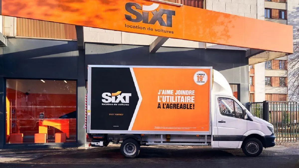 SIXT car rental agency in Bordeaux with a white van displaying the slogan 'I love making the useful agreeable' in front of the orange and black storefront.