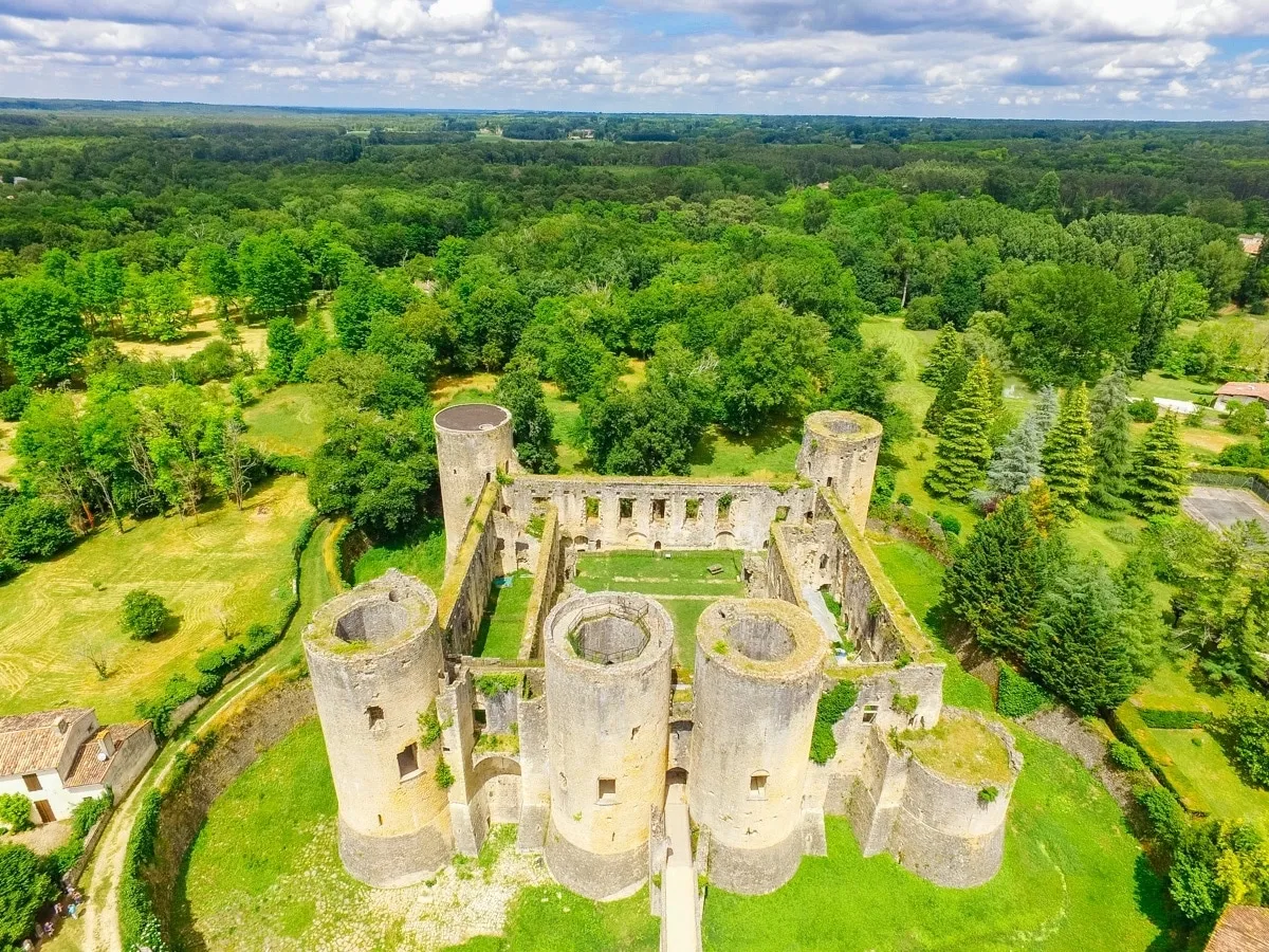 Aerial view of Château de Villandraut near Bordeaux, displaying its cylindrical ruined towers surrounded by green landscapes and forests.