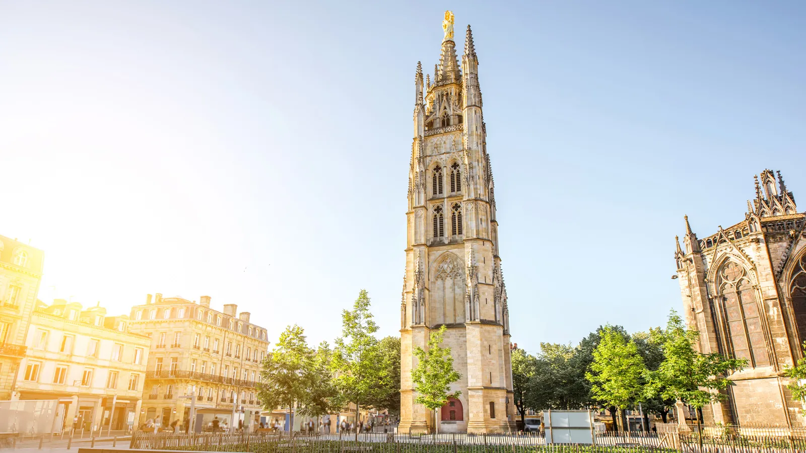 Pey-Berland Tower, a 15th-century Gothic bell tower in Bordeaux, featuring ornate spires and a golden statue on top, surrounded by historic buildings and trees.