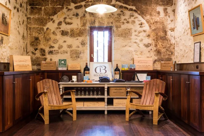 Interior of Château Paveil de Luze in Bordeaux featuring stone walls, two wooden armchairs, wine tasting counter, and wine bottles on display.