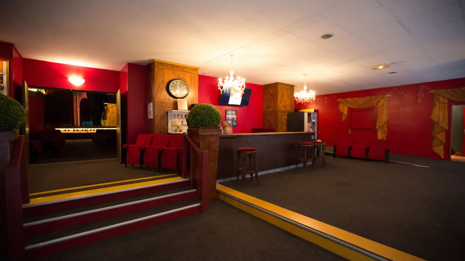 Entrance hall of the Salinières Theater in Bordeaux featuring red walls, wooden reception desk, red seats, crystal chandeliers and gold accents