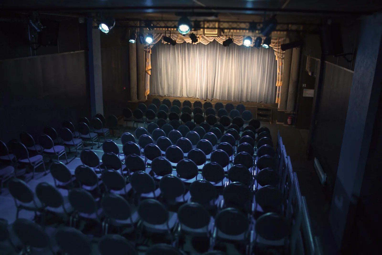 Empty theater auditorium at Bordeaux's Théâtre Victoire with blue seats arranged in rows, white curtain and stage lights