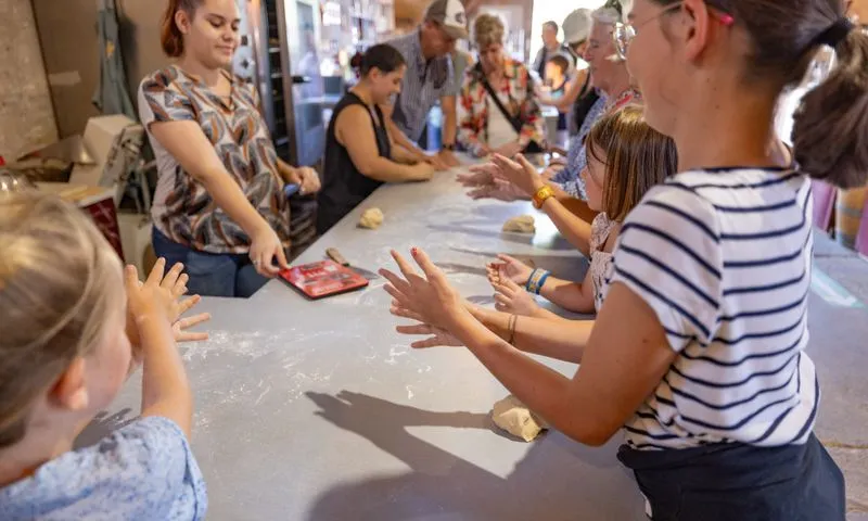 Cooking workshop at Moulin de Porchères in Bordeaux: children and adults preparing bread dough together at a work table.