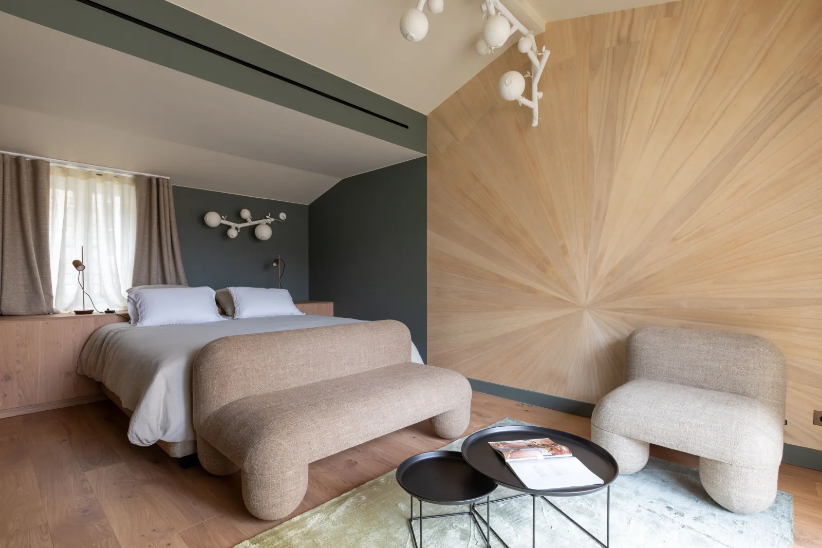 Modern bedroom at Yndo Hotel in Bordeaux featuring a king-size bed, dark grey walls, light wood paneling, contemporary beige furniture, and black side tables.
