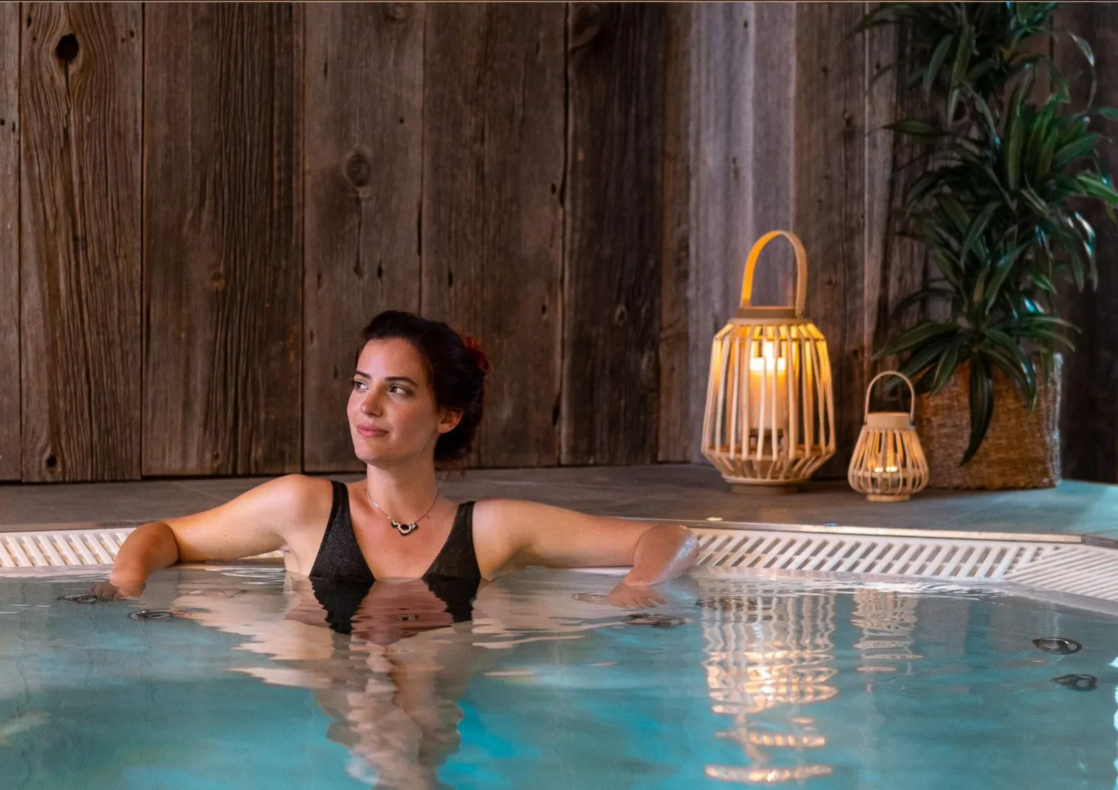 Woman relaxing in a turquoise thermal water pool at La Zoologie spa in Bordeaux, with wooden wall and bamboo decoration in the background