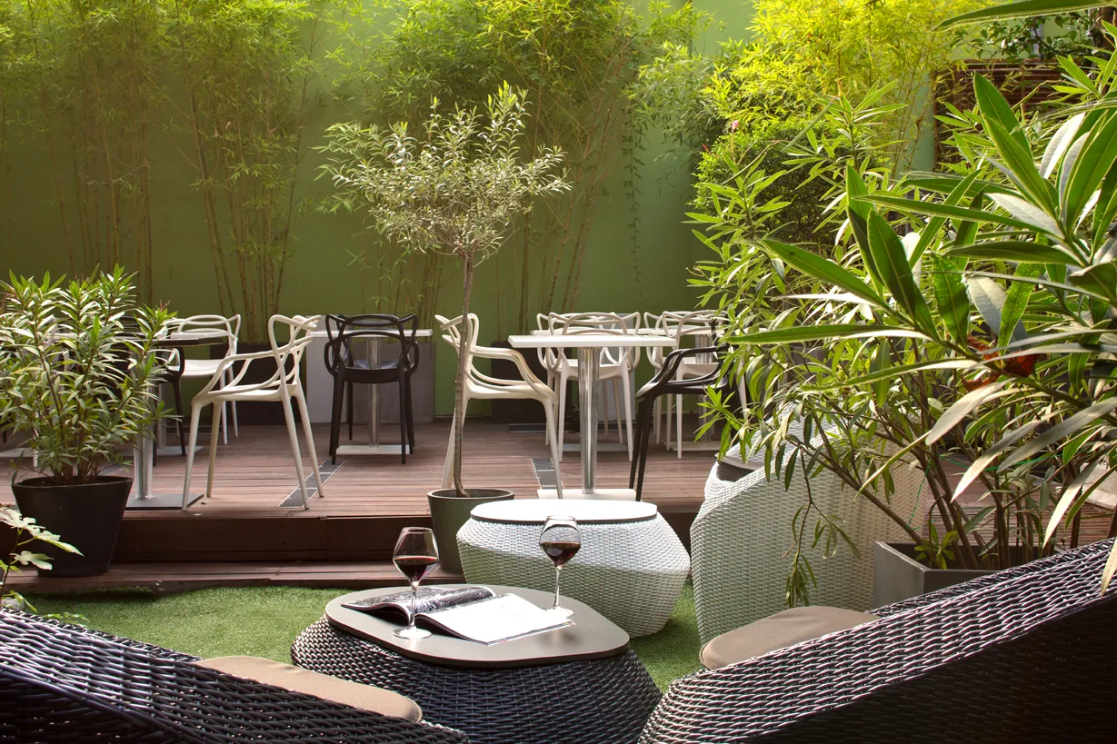 Elegant terrace of a boutique hotel bar in Bordeaux featuring designer furniture, potted bamboo plants, artificial grass, and relaxation areas surrounded by lush greenery.