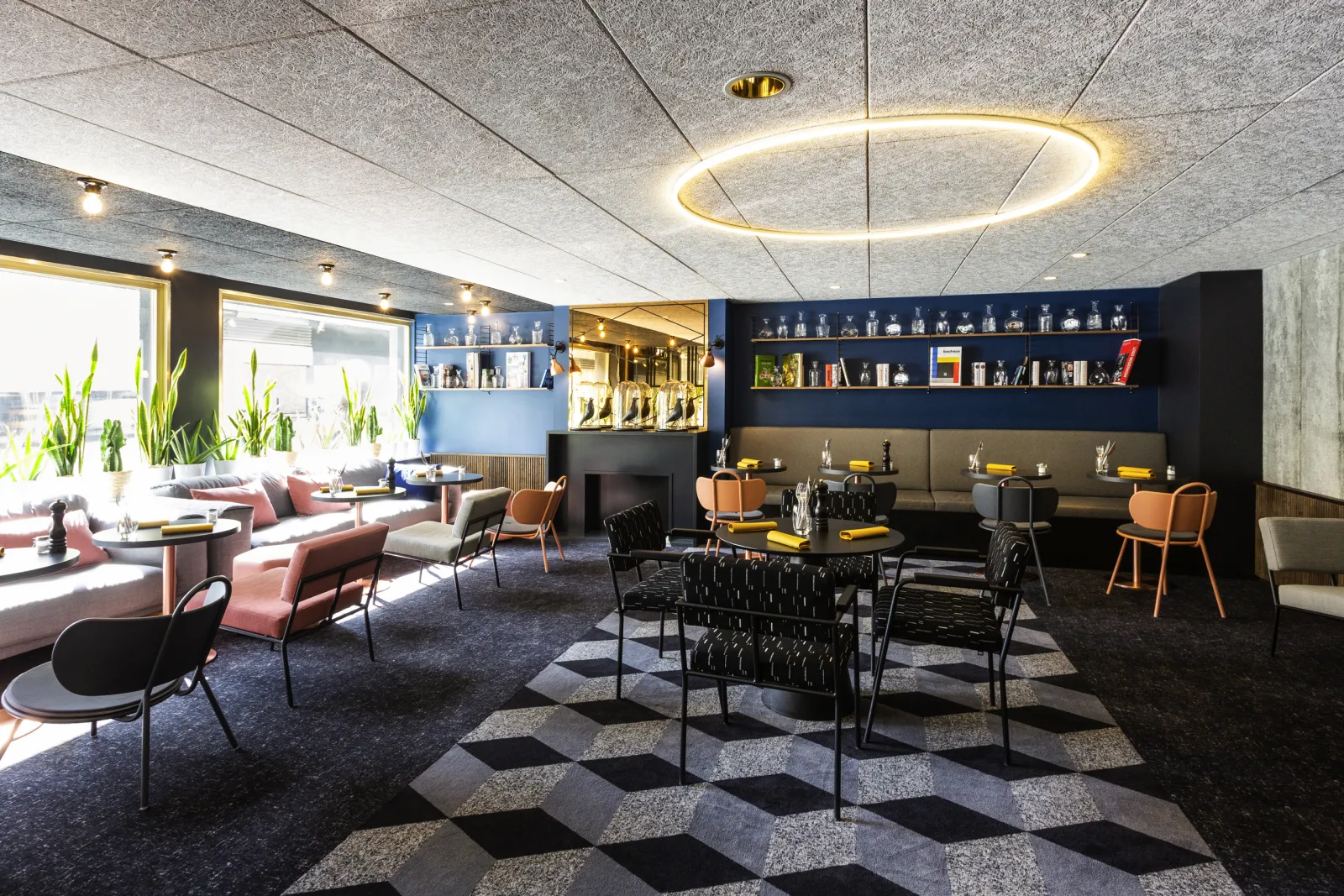 Modern lounge area at Mercure Bordeaux Centre hotel featuring contemporary furniture, wall shelving, bar counter, large windows and architectural concrete ceiling with circular golden lighting
