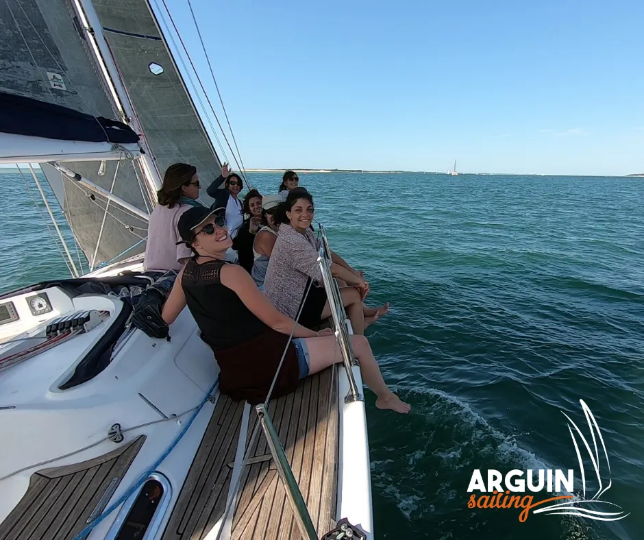 Group of passengers enjoying a sailing day near Bordeaux, sitting on the deck of the White Pearl sailboat with sails deployed and calm sea in the background