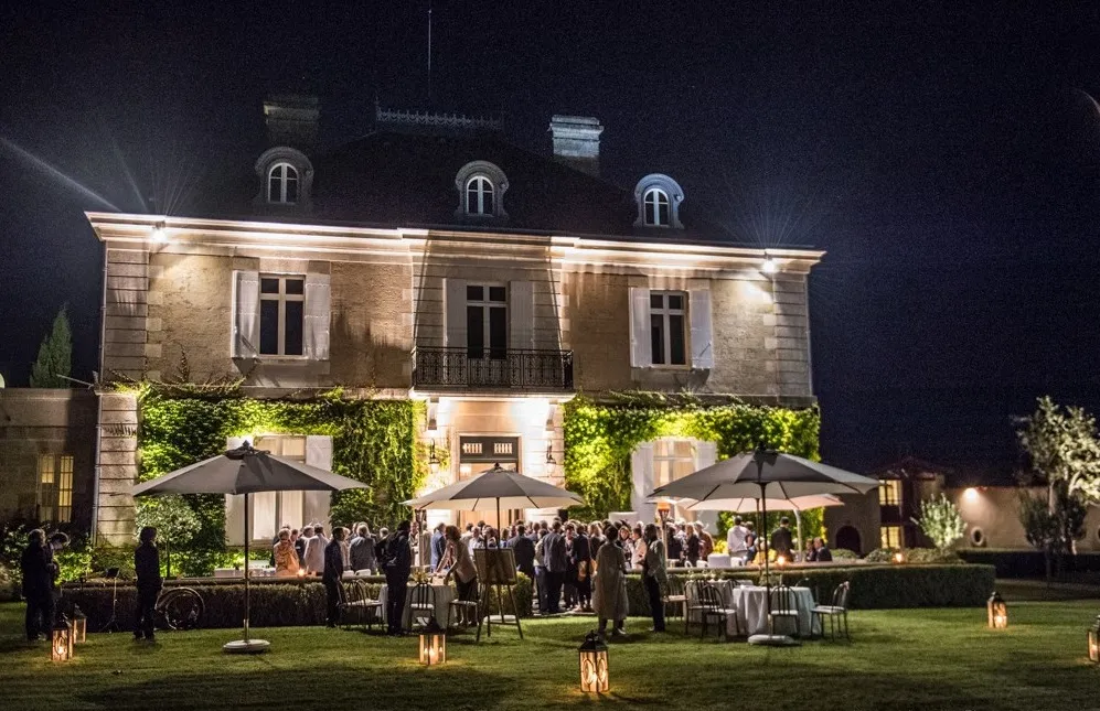 Night view of Château Haut-Bailly in Bordeaux lit up, with an elegant event in the garden under black umbrellas and lanterns
