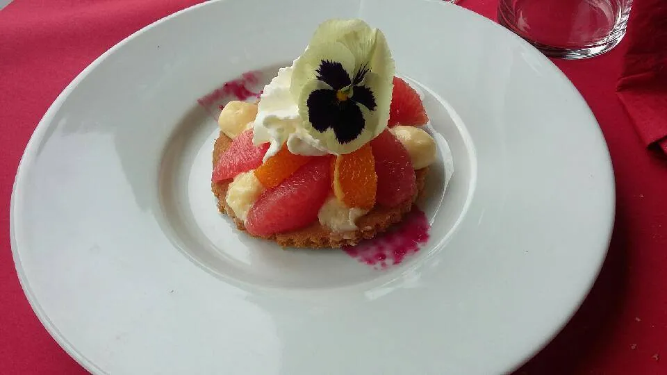 Elegant dessert featuring a red fruit and citrus tart topped with cream and edible pansy flower, presented at La Table de La Chèze in Bordeaux