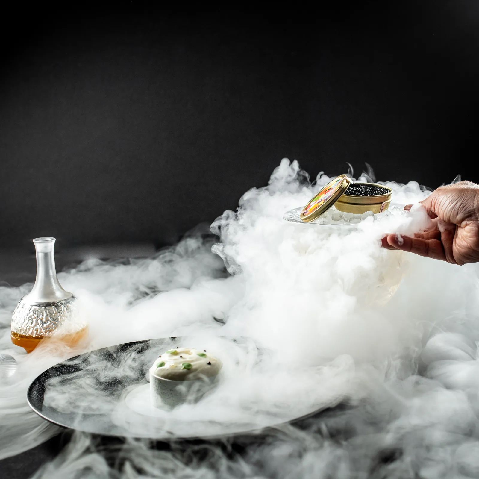 Fine dining presentation at Lalique restaurant in Bordeaux: plate with caviar and smoking egg, white wine glass and wedding rings in dry ice vapor cloud