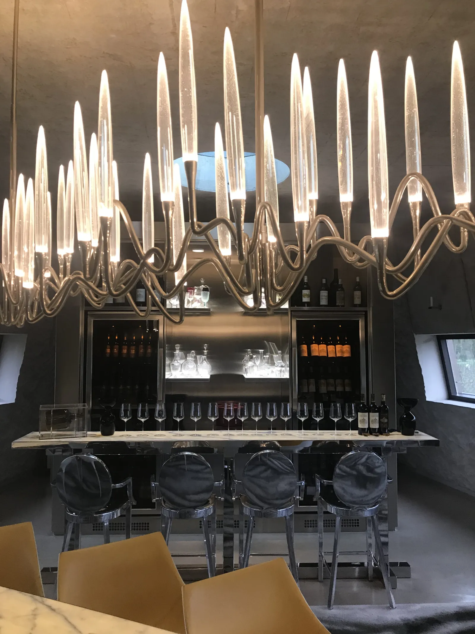 A modern bar with a black counter topped by a spectacular white neon spike-shaped chandelier, flanked by gray chairs, at Château les Carmes Haut-Brion in Bordeaux.