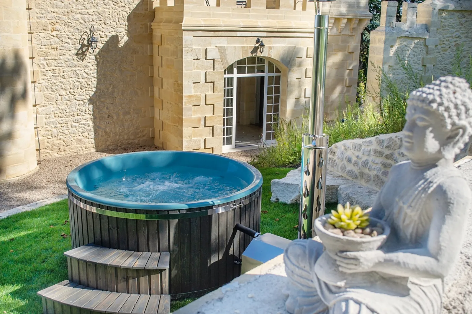 Turquoise inflatable hot tub in the courtyard of Château de Roques in Bordeaux, surrounded by stone walls, statues and classical architecture.