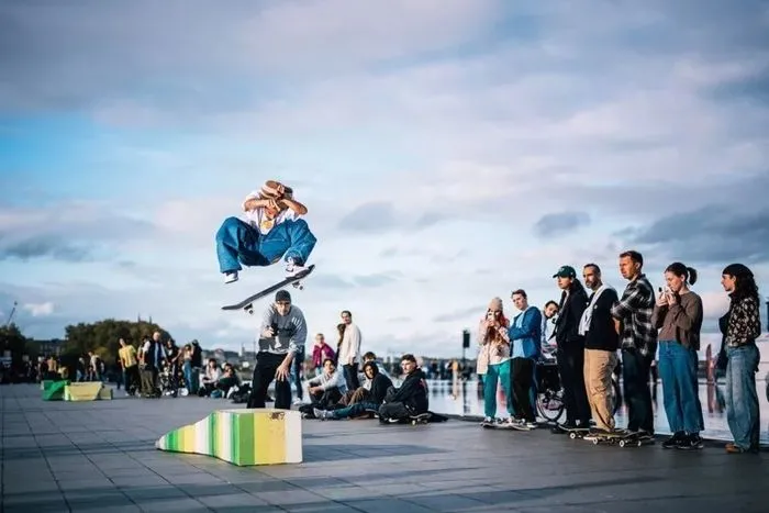 A skateboarder performs an aerial trick over a colorful ramp during the Connect festival in Bordeaux, in front of a crowd of spectators