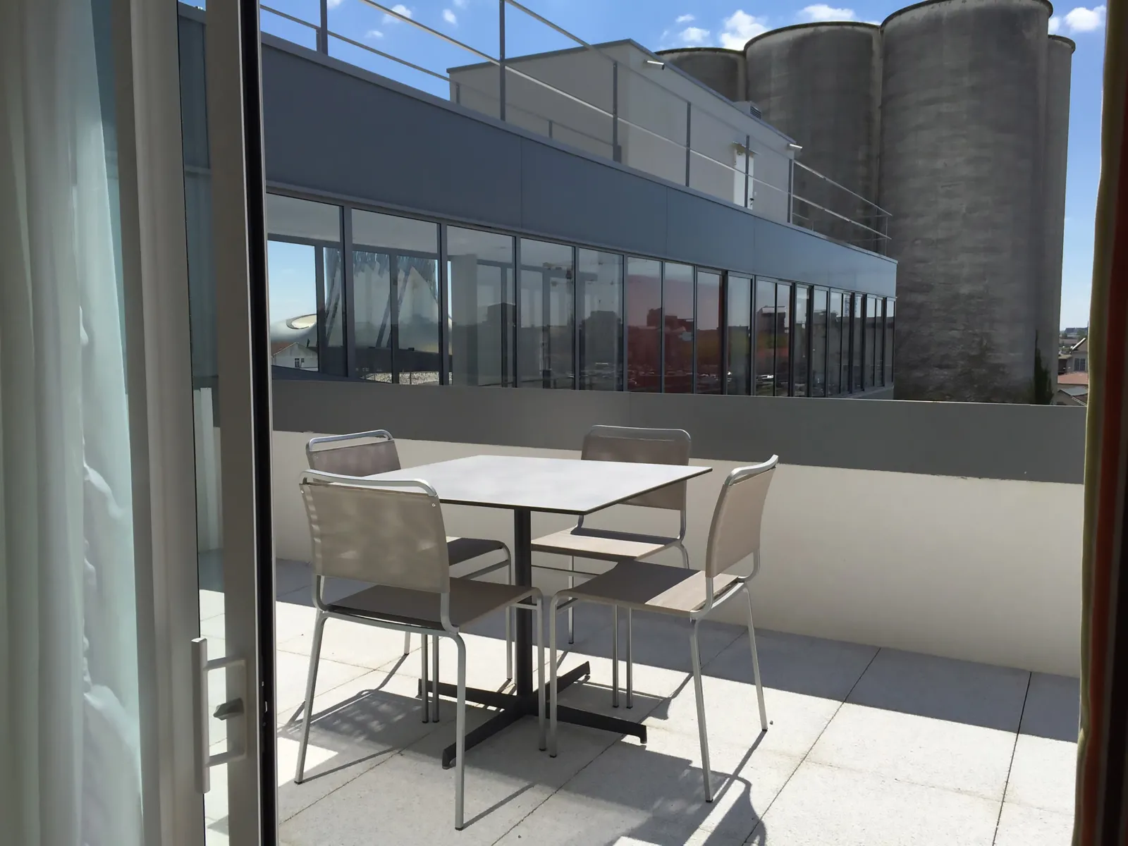 Sunny terrace of an aparthotel with table and chairs overlooking the Bordeaux Bassins à Flot and its distinctive silos