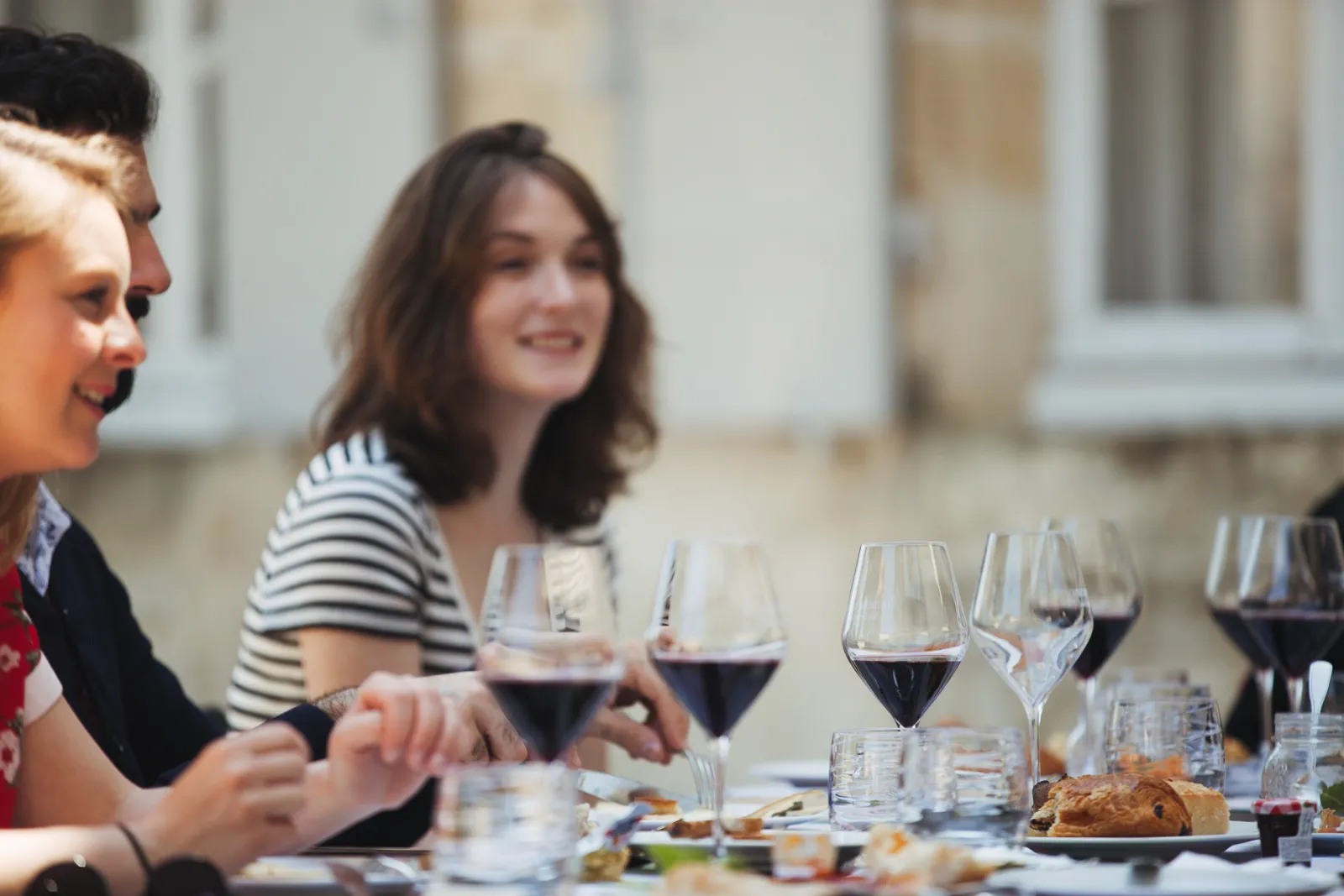 Group of people enjoying red wine tasting during an outdoor meal at Château Ambe Tour Pourret in Bordeaux, with wine glasses and gourmet dishes on the table