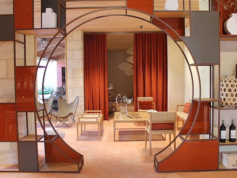 Interior exhibition of Château Marquis d'Alesme Becker in Bordeaux featuring a modern living room with designer furniture, red drapes, metal arches and contemporary decorative elements.
