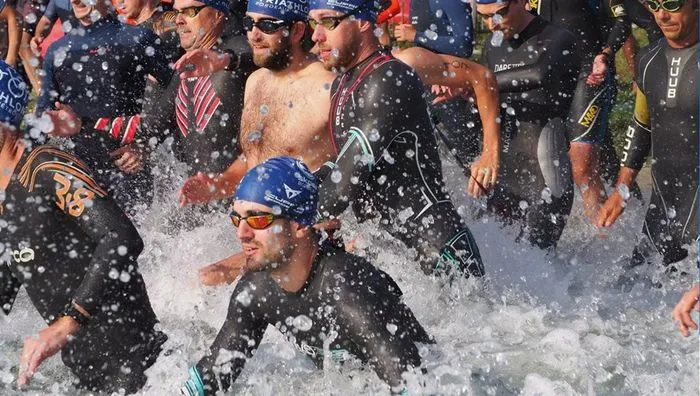 Group of triathletes exiting the water during the Bordeaux Triathlon, with water splashing, swimmers wearing wetsuits and goggles