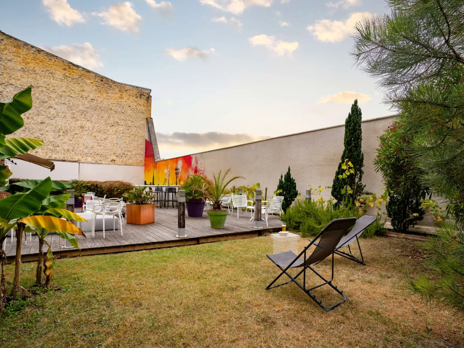 Outdoor terrace of Ibis Styles Bordeaux Centre Gare featuring a lounger in the foreground, landscaped garden, white sun loungers and colorful artwork on the elevated deck